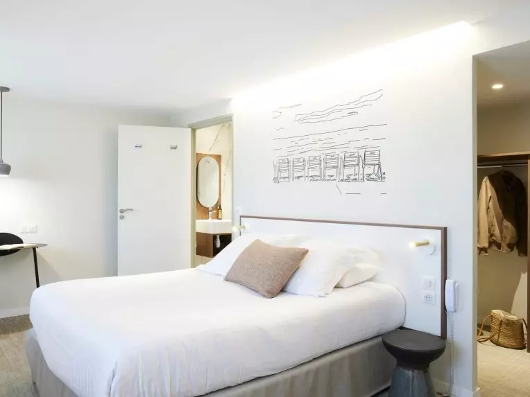 Chambre de l’hôtel du Pin à Nice avec lit king size, une illustration au mur de la promenade des anglais, vue sur salle de bain et dressing