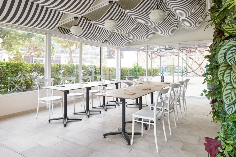 Vue d’ensemble sur la terrasse du restaurant Gigi Tavola Isidore à l’hôtel Isidore du Groupe Soniho avec une table en forme de U avec des carnets, stylos et verres posés dessus.