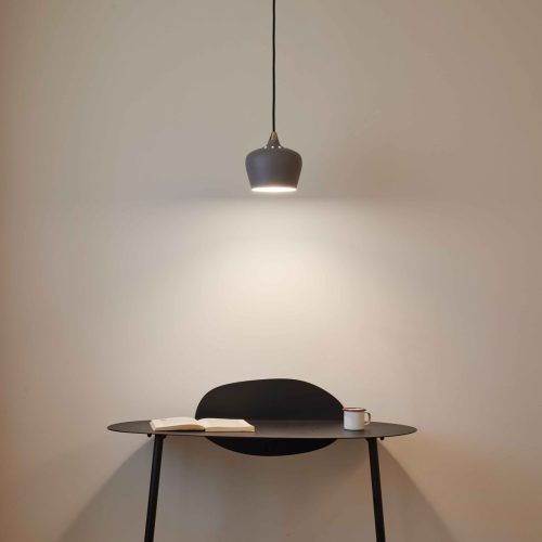 Modern, sleek, minimalist desk in a room at the Hotel du Pin in Nice with a green stool and a light fixture hanging with an open book and a cup of coffee.
