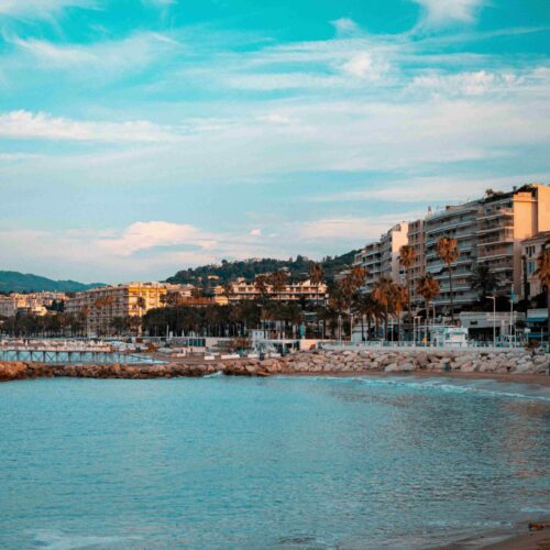 Vue de la Croisette à Cannes avec la mer bleue et des immeubles qui jalonnent la zone piétonne.