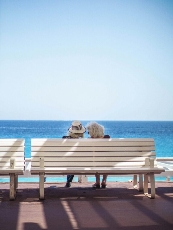 Célèbre banc blanc en plastique de la Promenade des Anglais à Nice, avec deux femmes d’âges mûrs de dos observant la mer.