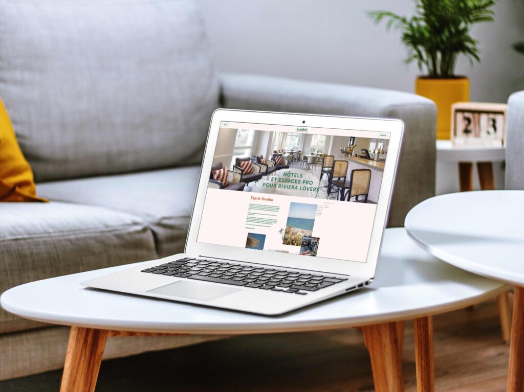 Page d’accueil du site internet du groupe hôtelier Soniho. Un ordinateur portable apple est ouvert et posé sur une table basse blanche dans un salon moderne composé d’un canapé gris.