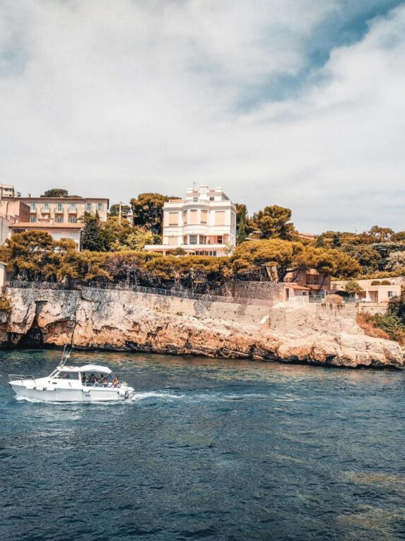 Un yacht passant devant la basse corniche sur la French Riviera bordé d’immeubles et de maisons typiques du Sud de la France