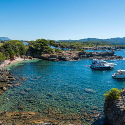 Une île de Lérins avec une crique de rochers qui borde la plage avec une eau turquoise de la mer Méditerranée avec des petits yachts.