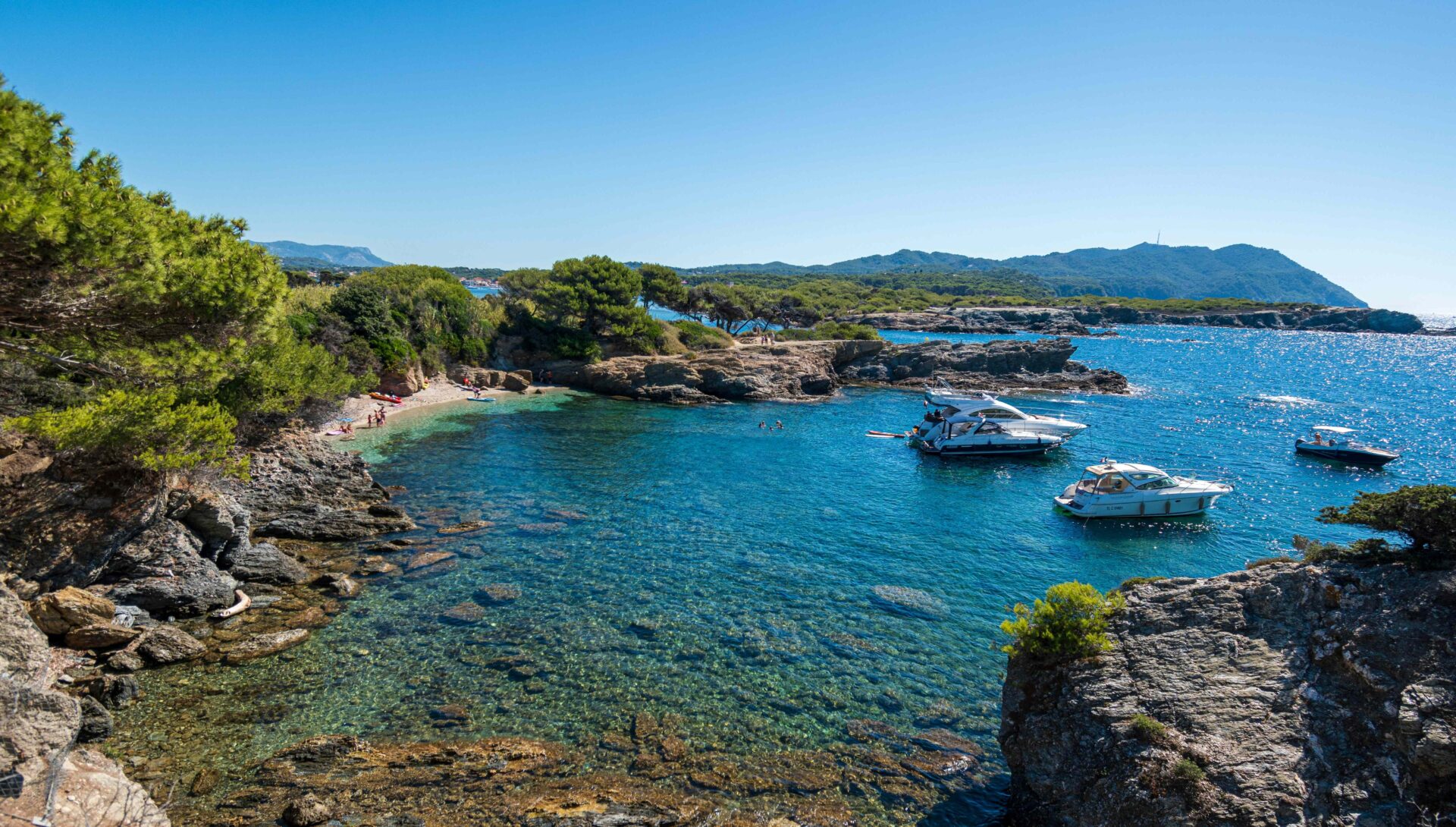 Une île de Lérins avec une crique de rochers qui borde la plage avec une eau turquoise de la mer Méditerranée avec des petits yachts.