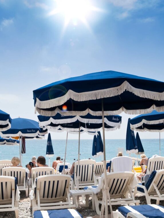 Sunny beach with blue umbrellas and deckchairs facing the Mediterranean Sea - summer atmosphere and seaside relaxation, ideal to illustrate a dream vacation on the Côte d'Azur.