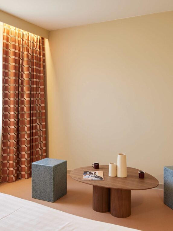 A hotel room with a warm, minimalist design, natural light, graphic curtains and contemporary furnishings - perfect for cosy, modern accommodation.