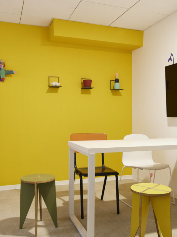 Creative, original space with bright yellow wall, colorful furniture and wall screen - perfect for dynamic meetings, brainstorming sessions or professional interviews.