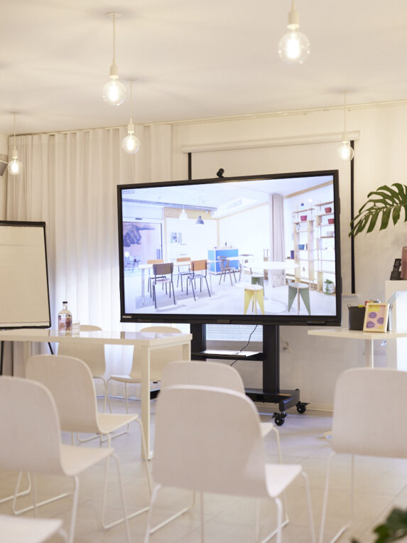 Scool Hôtel du Pin's “Salle Blanche,” a bright training room with rows of white chairs facing a large screen on wheels, and a flip chart on the side.