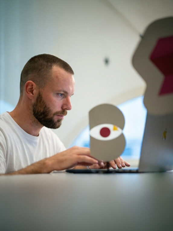 Homme concentré travaillant sur un ordinateur portable, assis à une table dans un environnement intérieur lumineux